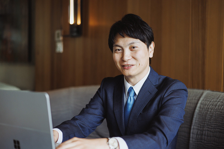 ノートパソコンを前に笑顔で話すスーツ姿の男性